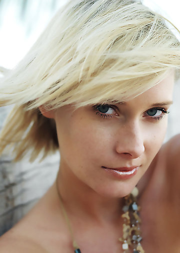 Girl with blonde hair displays small boobs and trimmed pussy on the palm tree